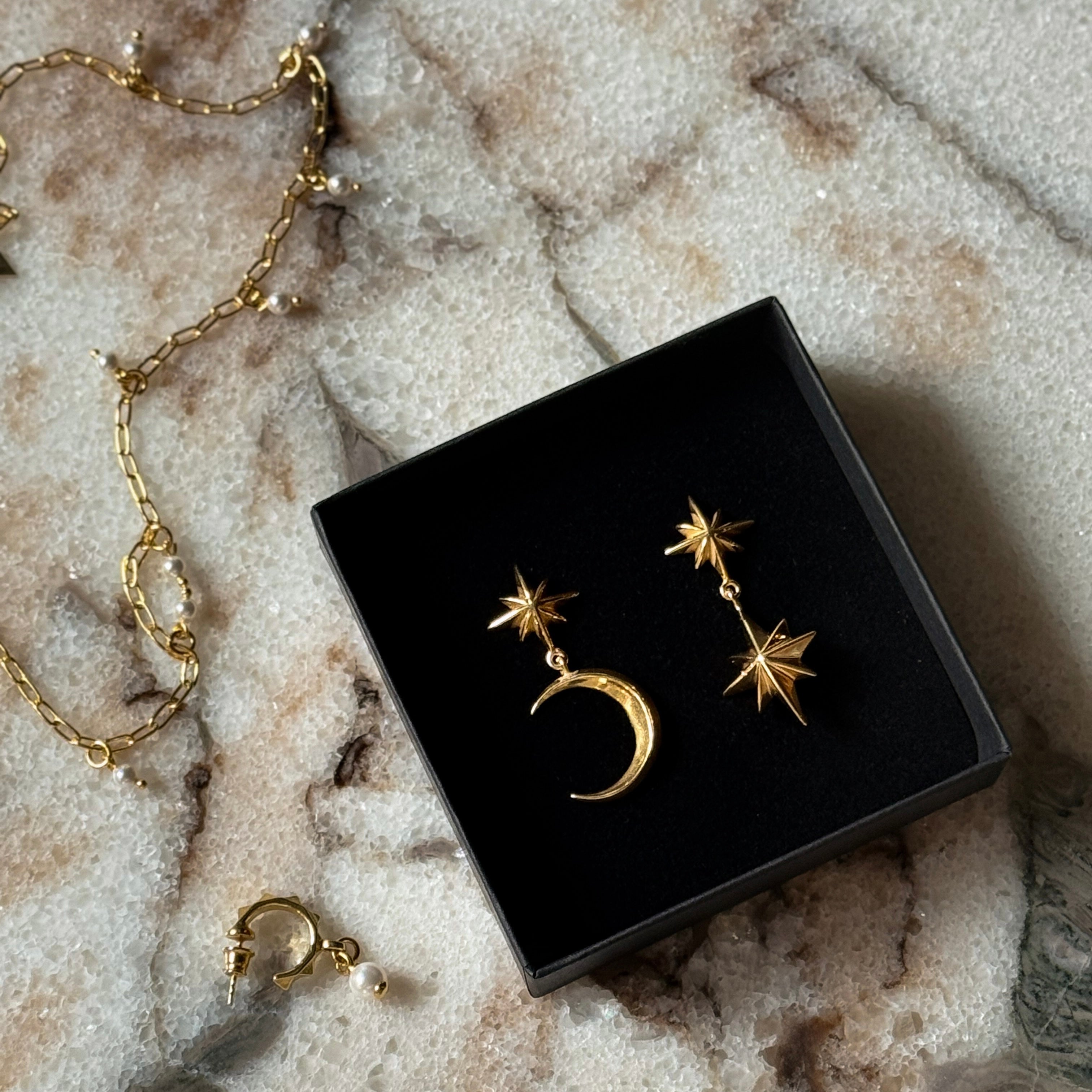 Dusk earring and Castor and Pollux earring by Macabre Gadgets in gold placed in a jewelry box, on white marble surface.
