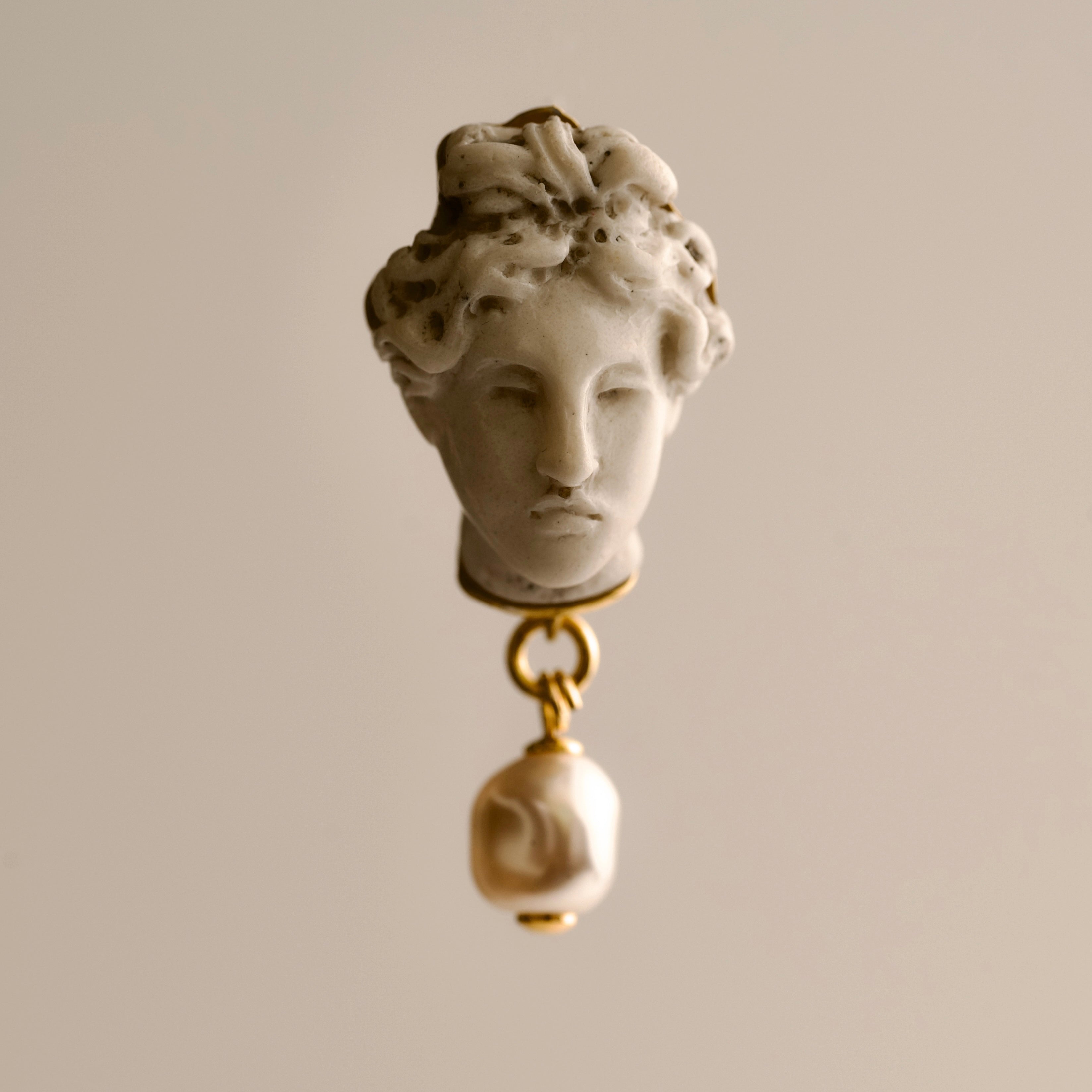 Aphrodite earring - hellenistic sculpture statement studs with classical head design and pearl on a beige background