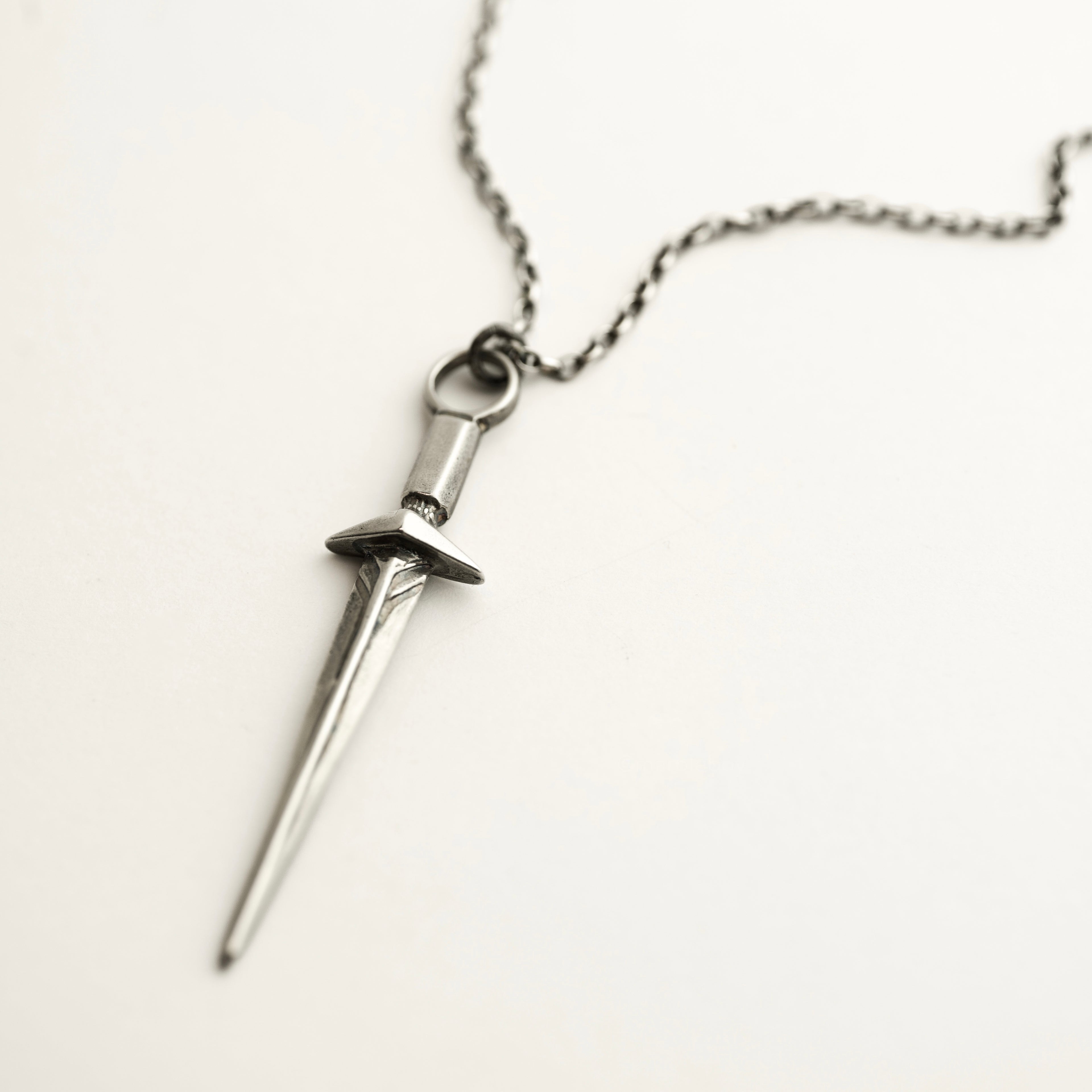Silver sword-shaped medieval or elven-inspired pendant on a chain against a light background