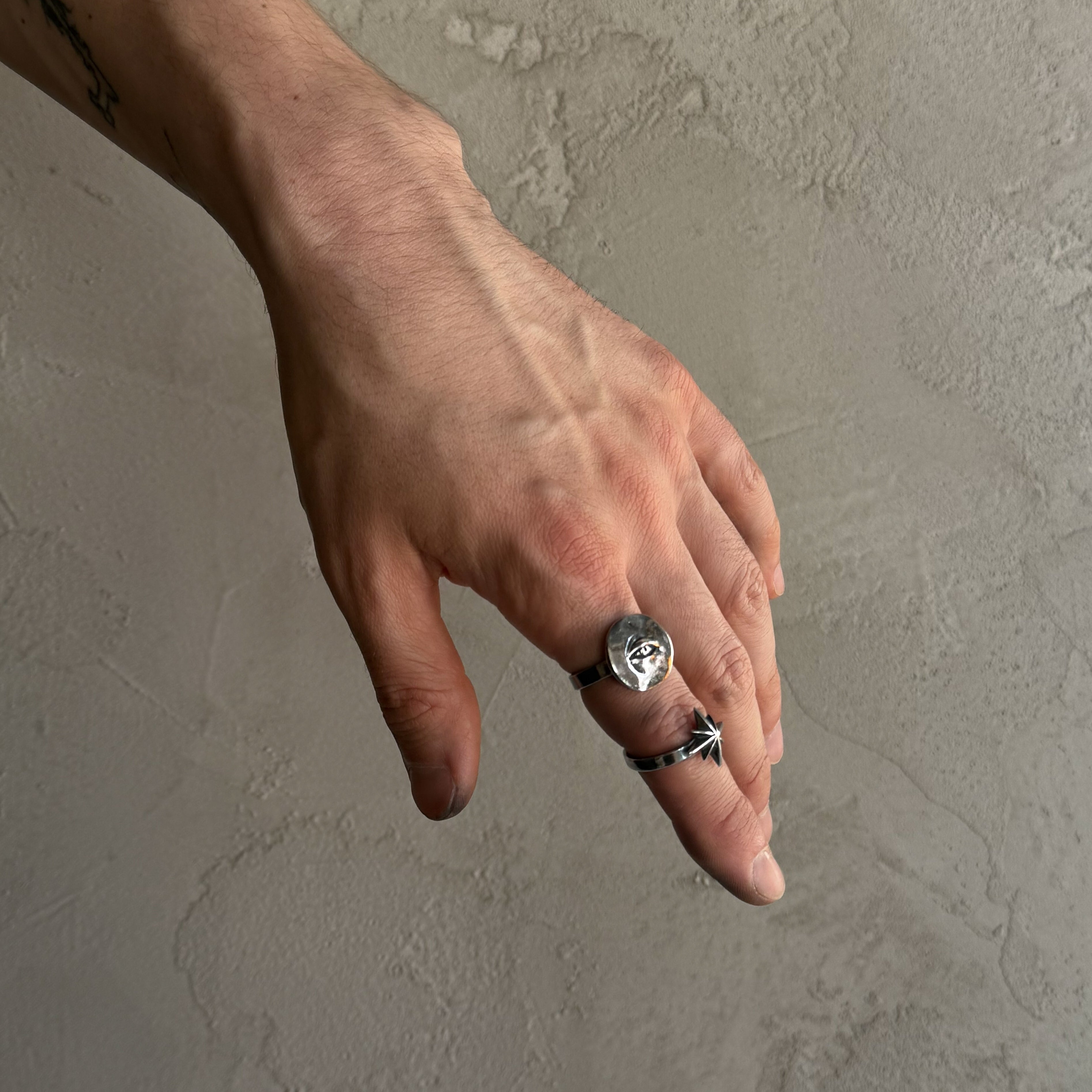 Star ring and Oculus ring on a male model's hand, focus on a shiny rings surface