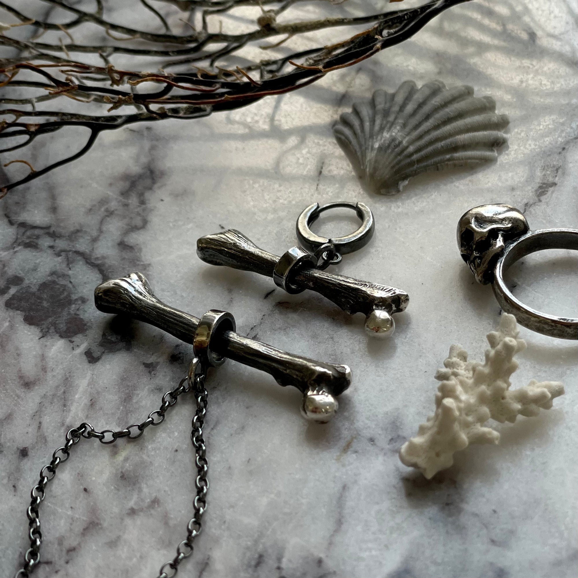 Silver Bone earring along with other jewelry placed on a stone surface surrounded by seashells and twigs 