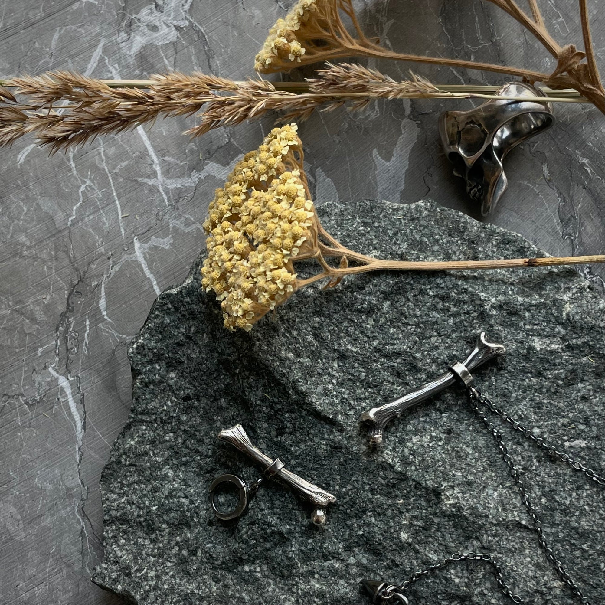 Silver Bone earring on a grey stone with other jewelry and cut flowers 
