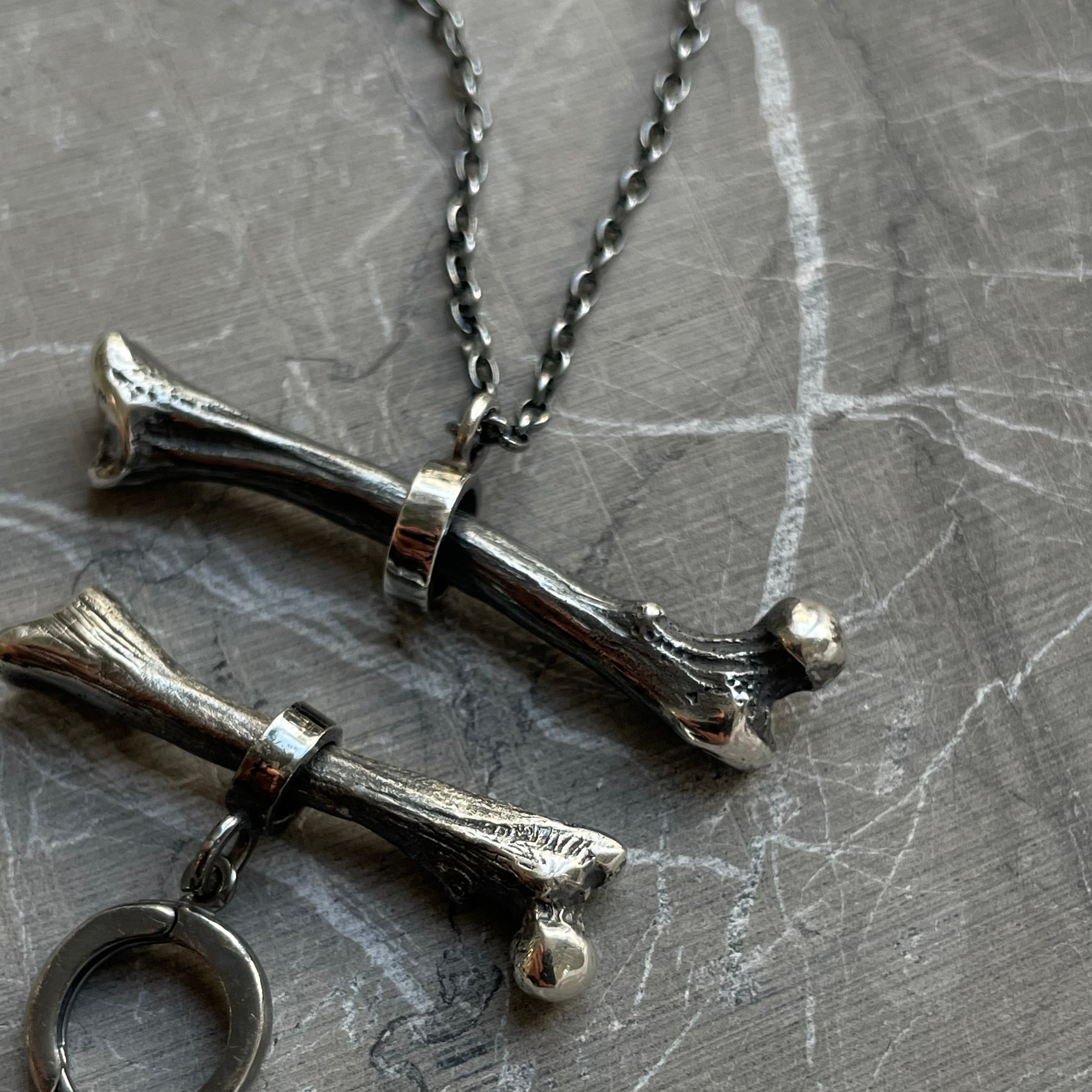 Silver Bone earring together with Silver Bone pendant placed on dark marble surface 