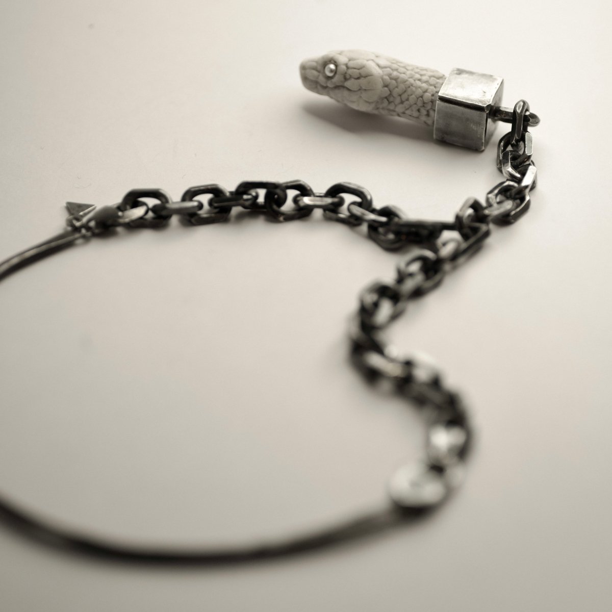 Aspis Snake necklace - white variant - placed on a white surface, focus on the bezel setting and anchor chain