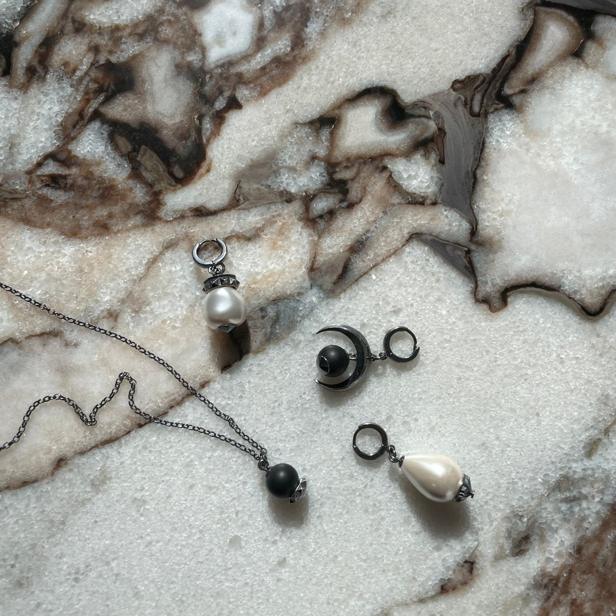 Baroque pearl earring, Moon earring and Blueberry pendant by Macabre Gadgets on a marble surface