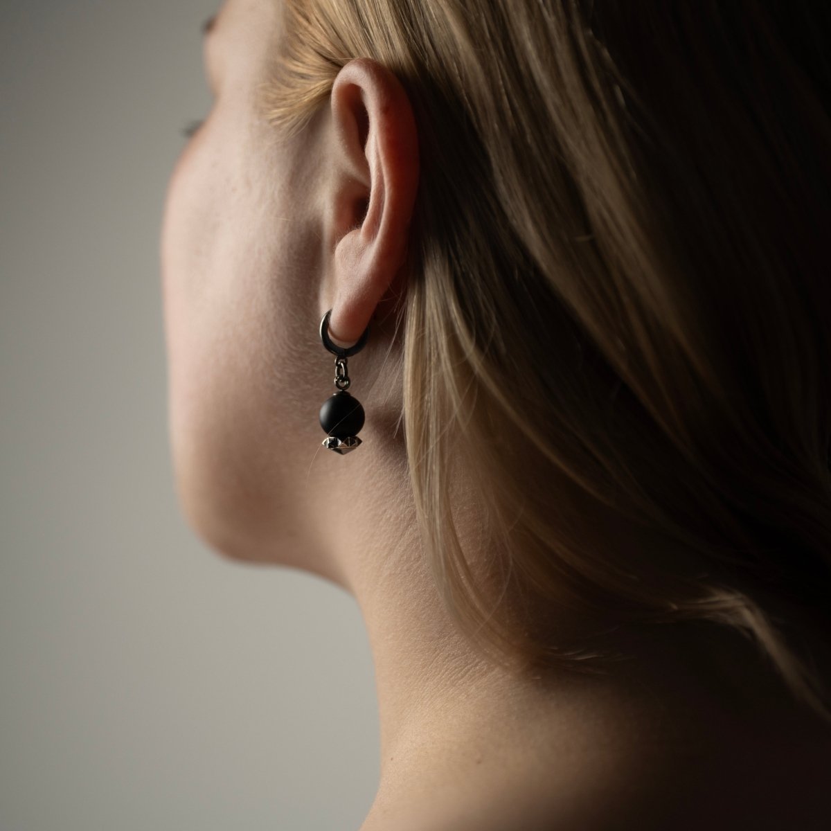 Female model with blonde hair wearing Blueberry earring silver variant, black onyx gothic jewelry lifestyle shot