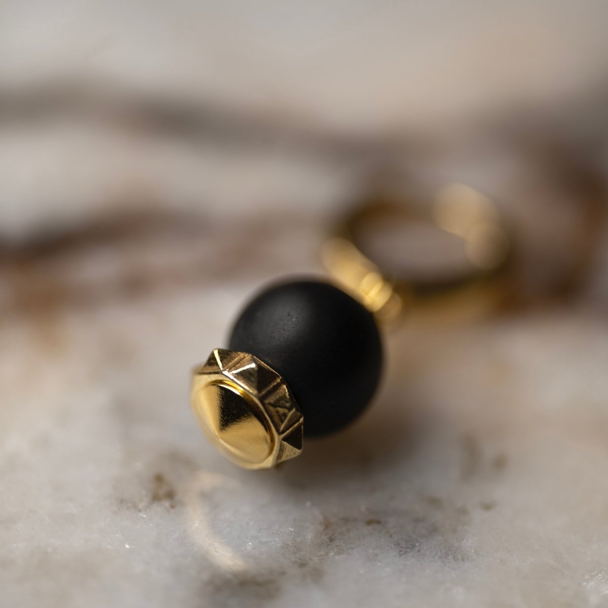 Blueberry earring gold-plated variant on marble surface showing black onyx stone with gold details, gothic jewelry
