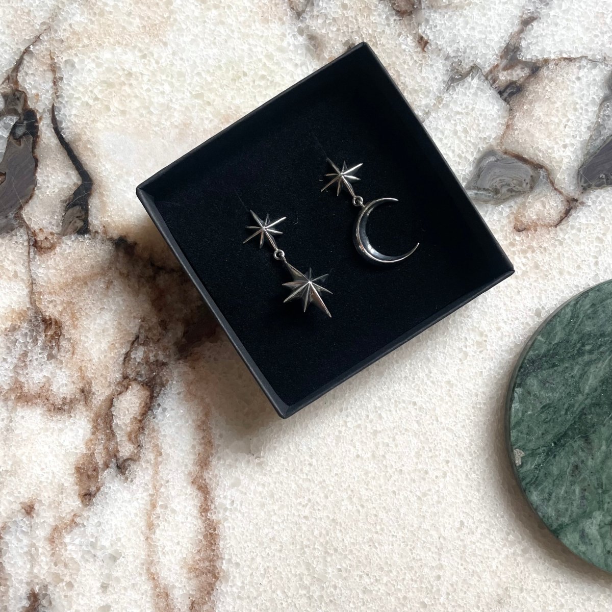 Castor & Pollux earring along with Dusk earring by Macabre Gadgets in jewelry box, on white marble surface