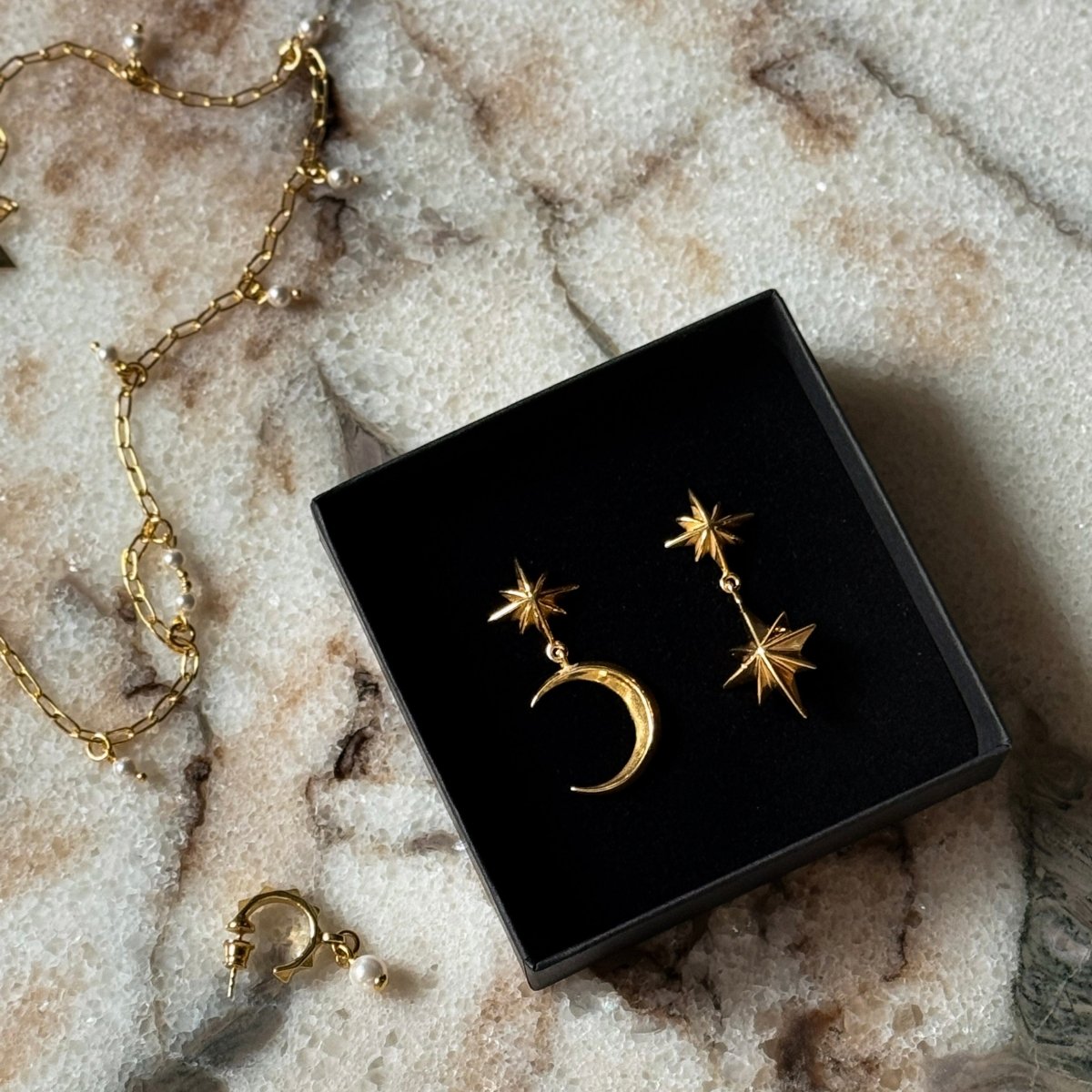 Castor & Pollux earring and Dusk earring - gold variant - in jewelry box, on white marble surface