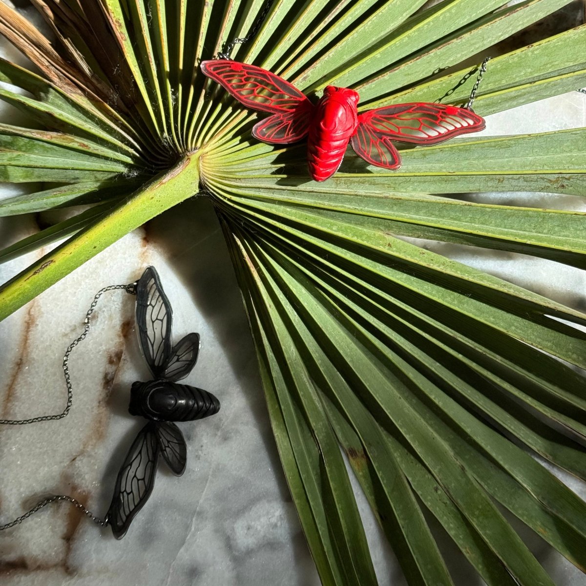 Cicada necklace - red and black variants - on a large palm tree branch with contrast warm light