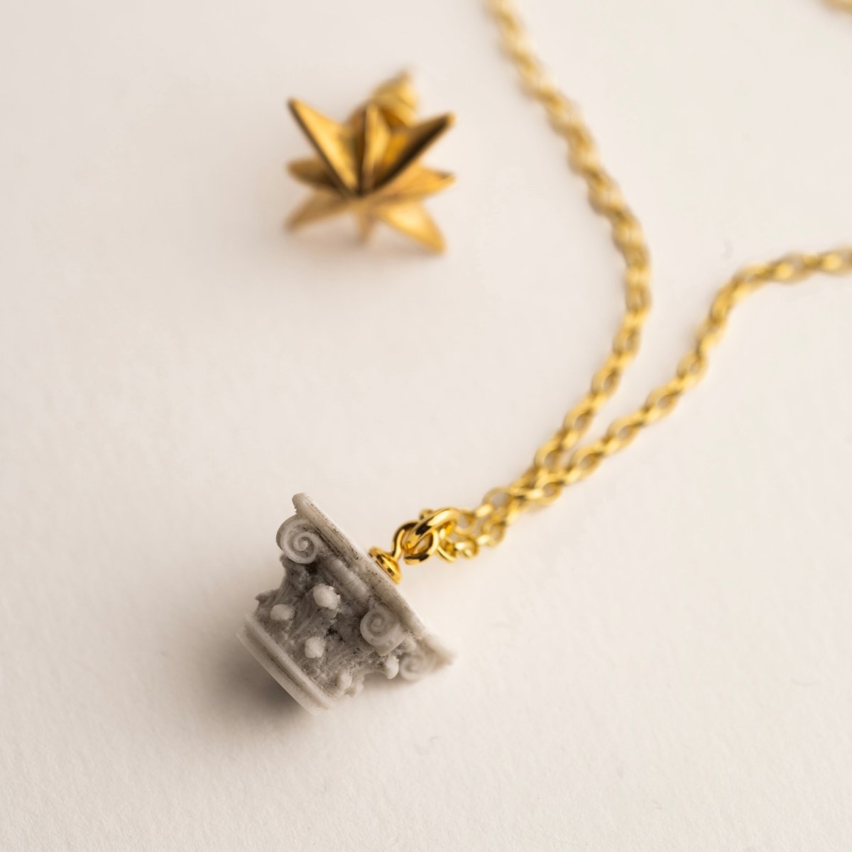 Corinth pendant and Star Stud earring on white surface, details and chain are visible