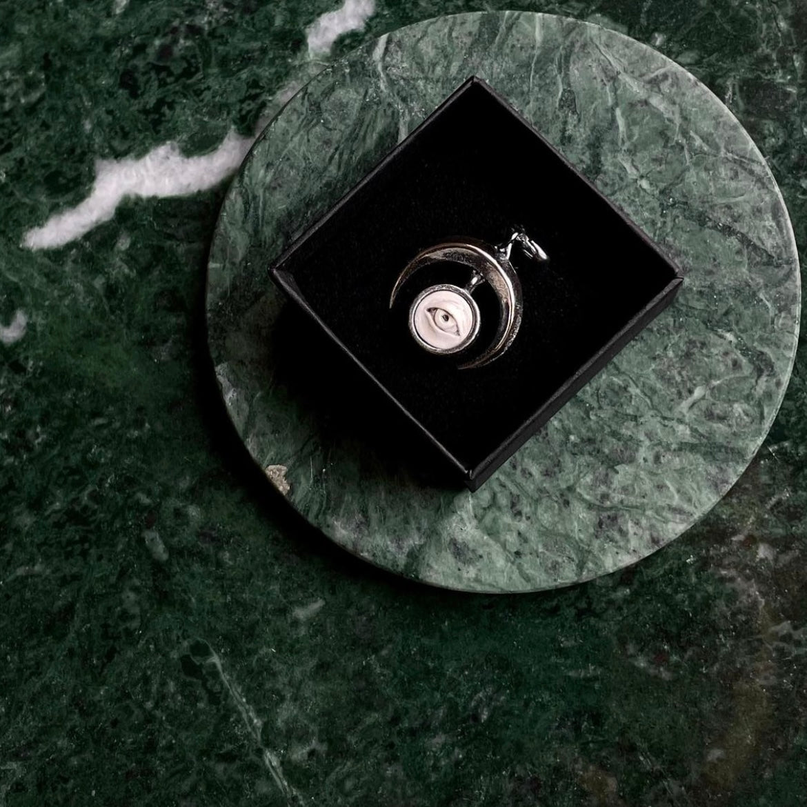 Crescent Oracle earring in luxury black jewelry box on green marble surface, gothic astrology jewelry presentation