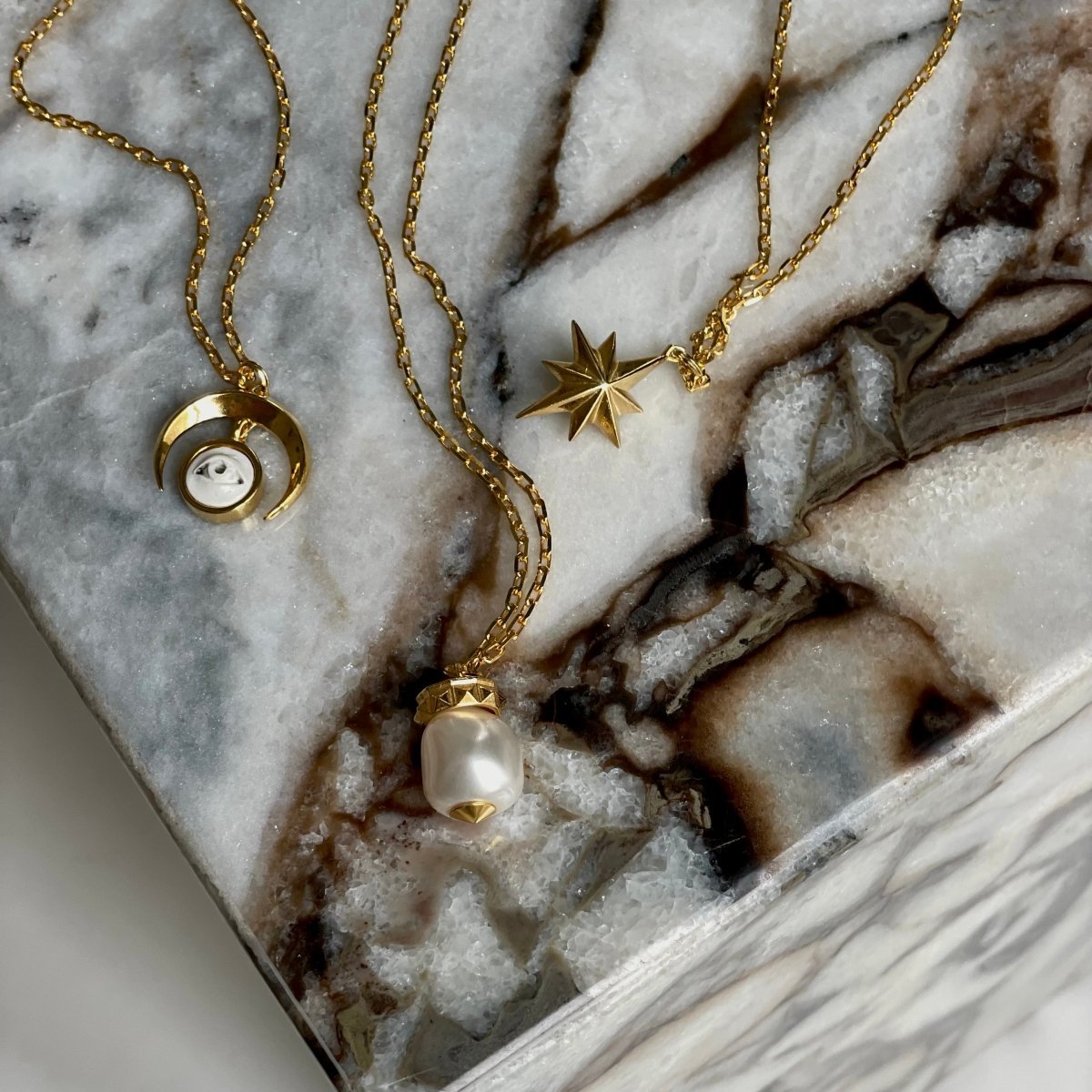 Crescent Oracle pendant - gold variant - along with other chain necklaces by Macabre Gadgets on a white marble surface