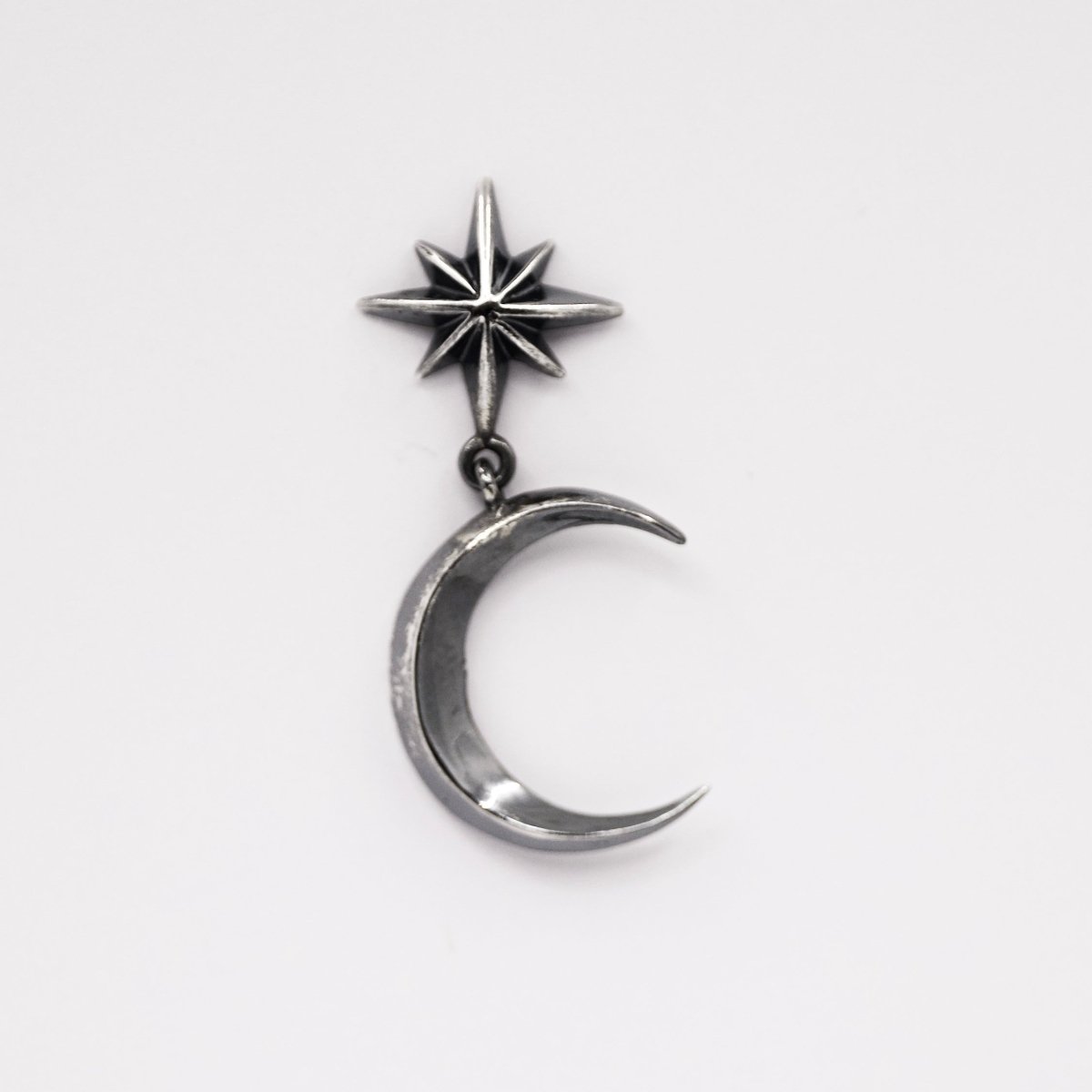 Dusk earring by Macabre Gadgets with sterling silver star and crescent moon design on neutral background, celestial jewelry