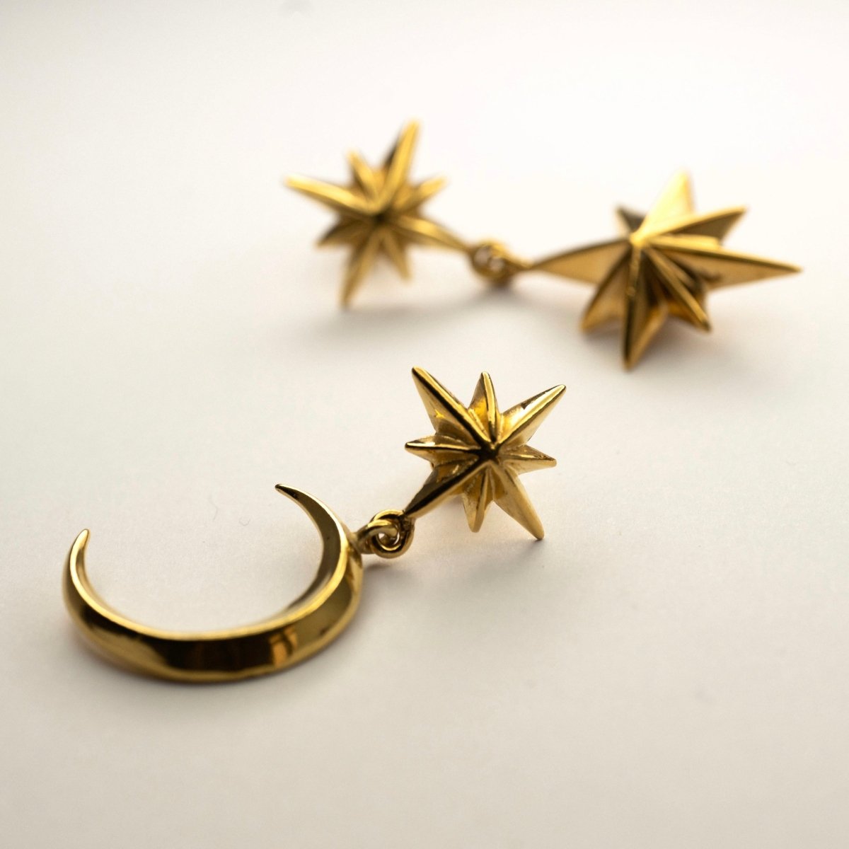 Dusk earring - gold variant - on a white surface with Castor and Pollux earring on a neutral background
