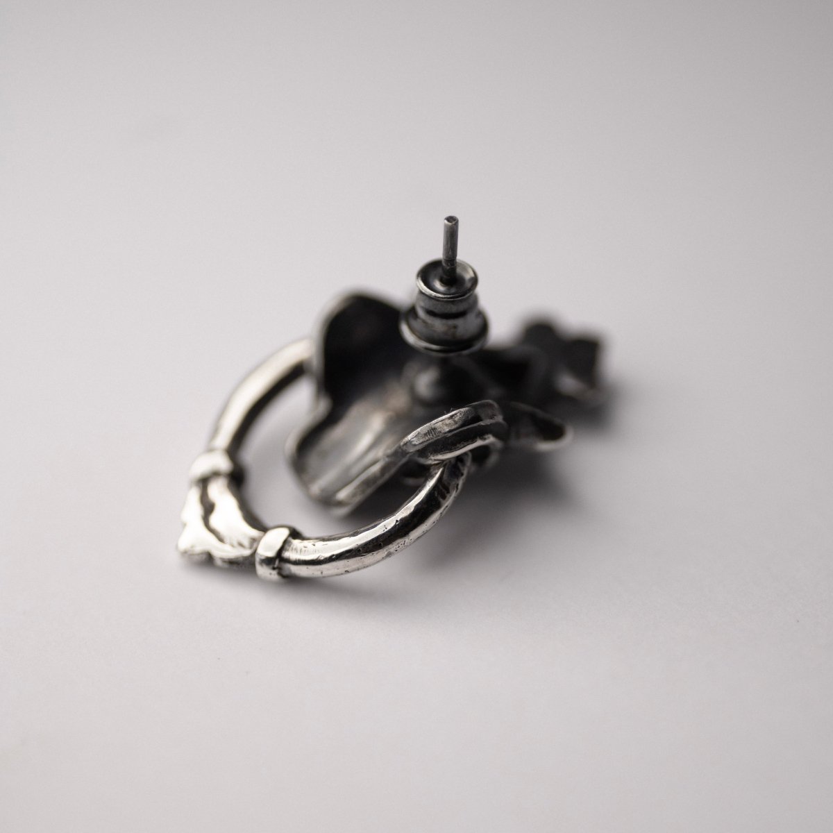 Silver Mask earring - placed upside-down on a white surface with stud lock clearly visible