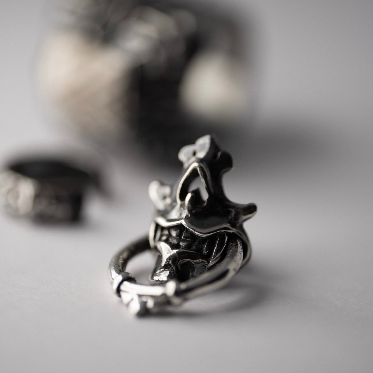 Silver Mask earring on a surface with other jewelry blurry on a background