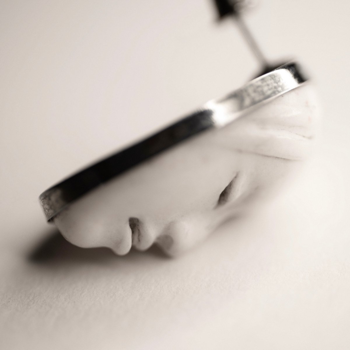 Mask earrings - white earring on a white surface, blackened sterling silver detail creates striking contrast with the tone of the picture