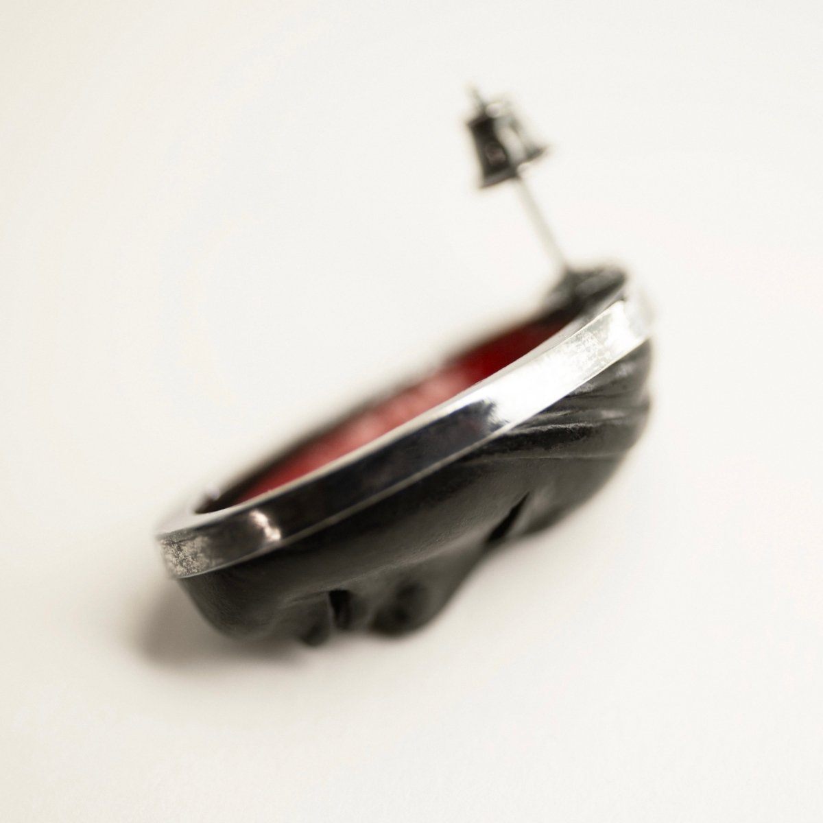 Mask earrings - black variant - shown on a white surface on a side, with a bit of red interior visible