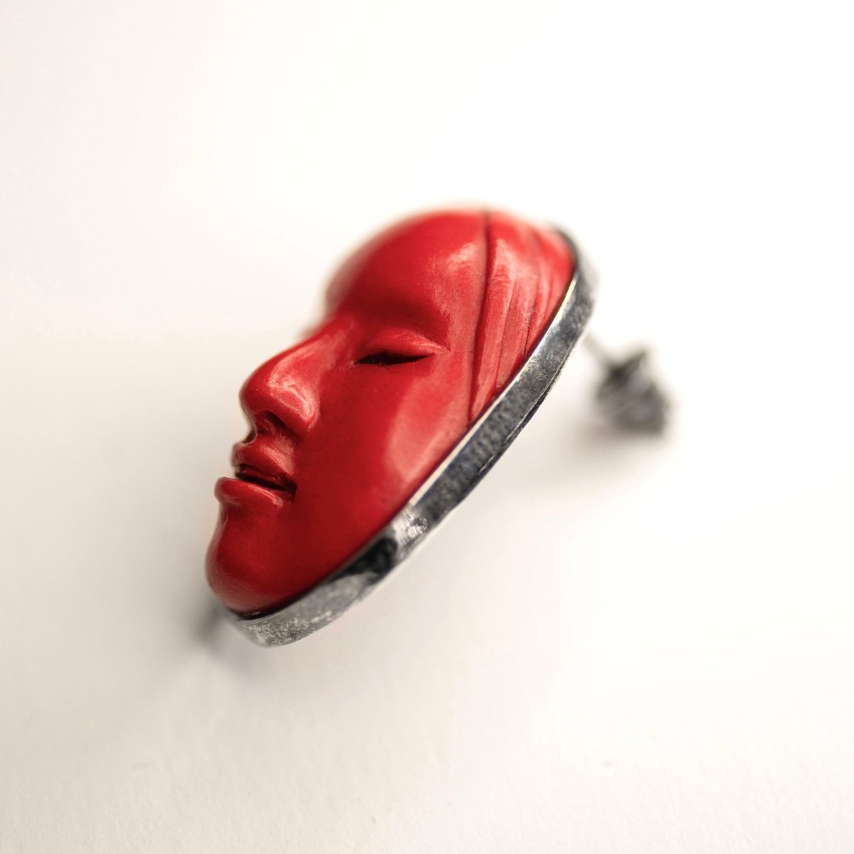 Mask earrings by Macabre Gadgets - red earring placed on a white surface
