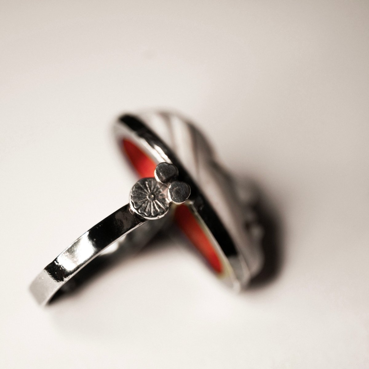 Mask ring - white variant - on a white surface on its side, focus on sterling silver part of the ring, yet blurry - we can see both white exterior and red interior of the mask part