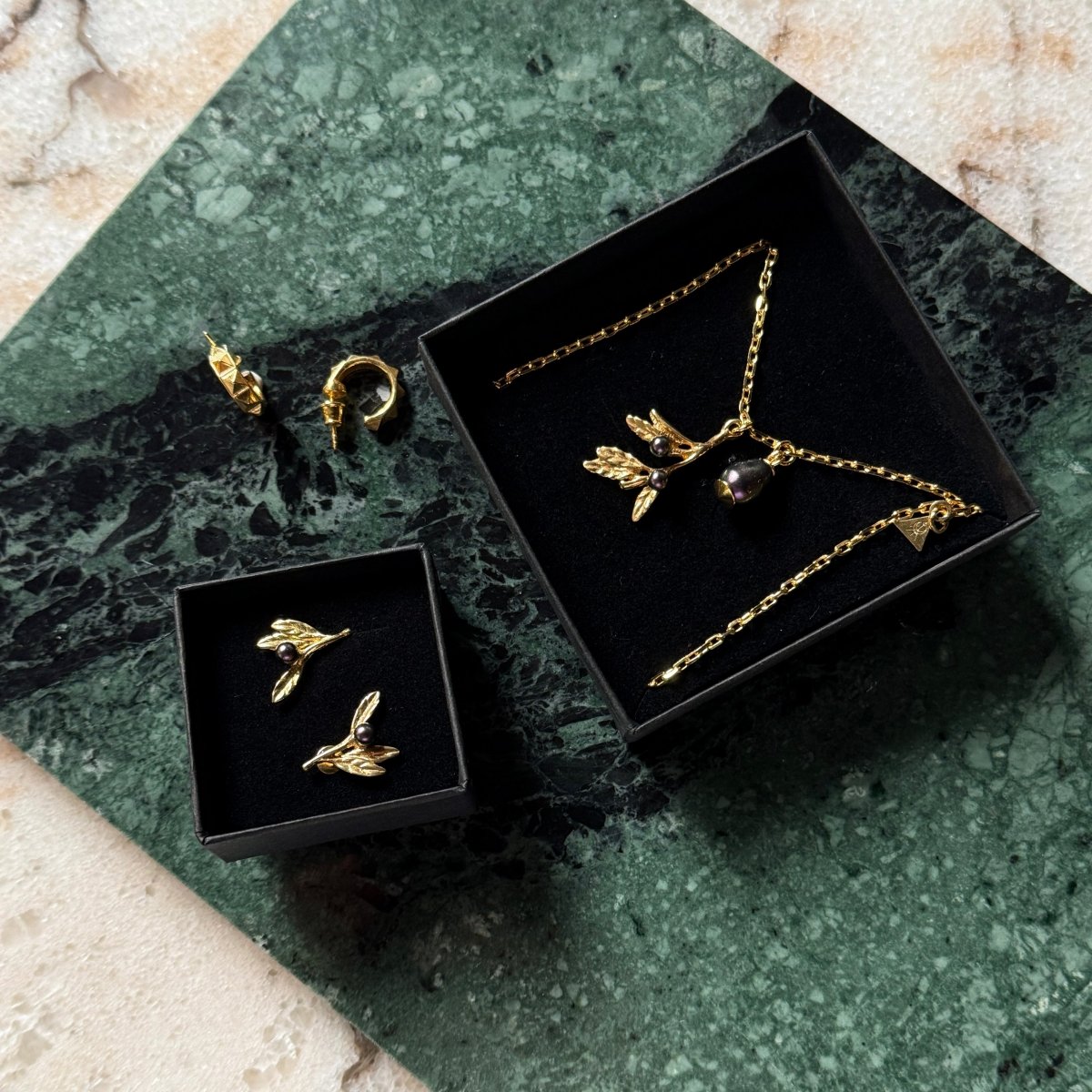 Olive Branch pendant in a jewelry box along with Olive branch earrings by Macabre Gadgets placed on a slub of green marble
