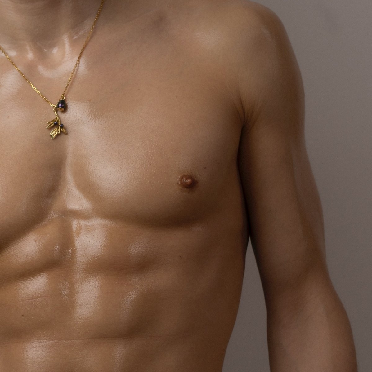 Olive Branch pendant - gold variant - on a male model with glossy skin, overall palette of the image is beige and neutral