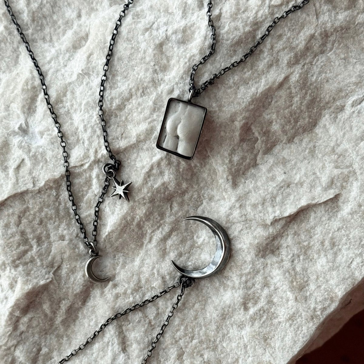 Selene Moon pendant, Luna pendant and Marble Fragment pendant on a raw marble surface