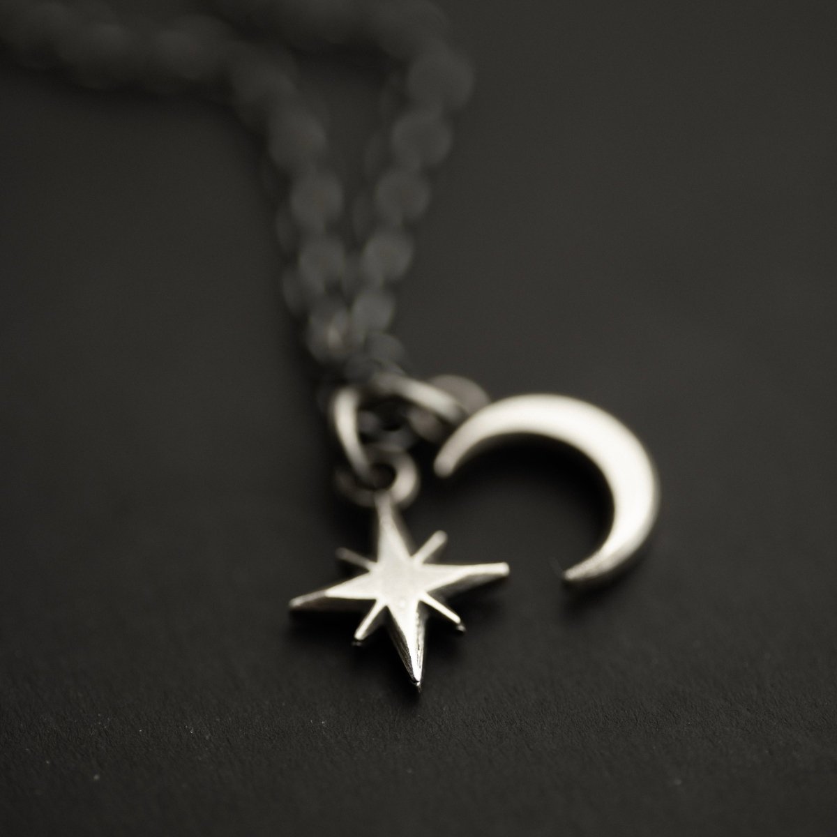 Selene Moon pendant and Asteria Silver Star pendant lying on the black surface shining like true celestial bodies in the night sky