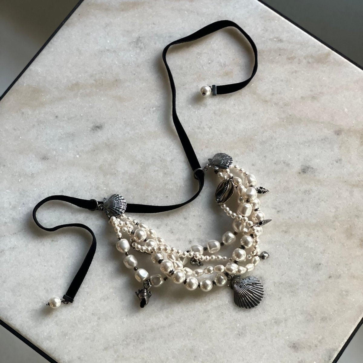 Siren Pearl Necklace placed on a marble table, size adjustable lace is visible