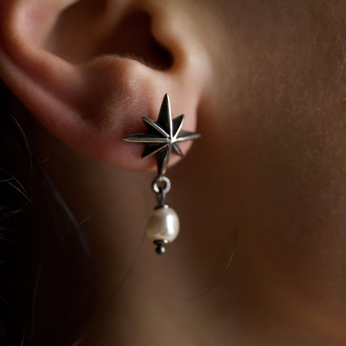 Star & Pearl earring close-up on model's ear, handcrafted sterling silver star with glass pearl detail