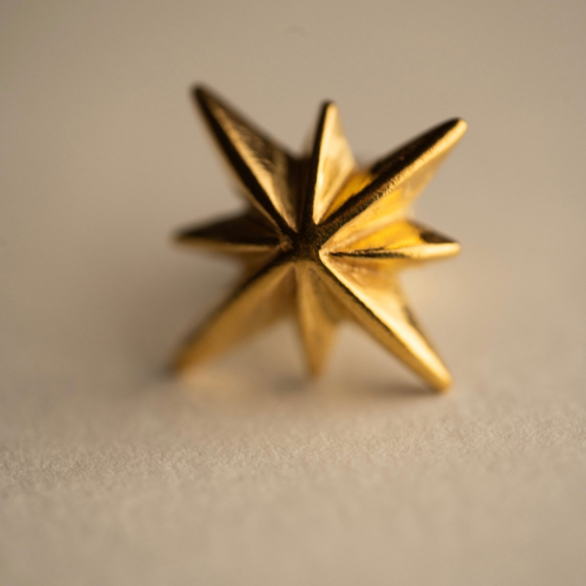 Star stud earring gold variant on beige surface close-up, handcrafted celestial jewelry detail