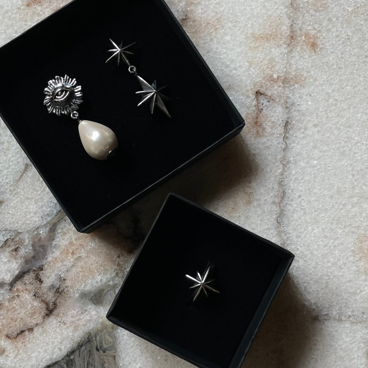 Star stud earring, Sirius Pearl Drop earring and Castor and Pollux earring in black jewelry boxes on white marble surface