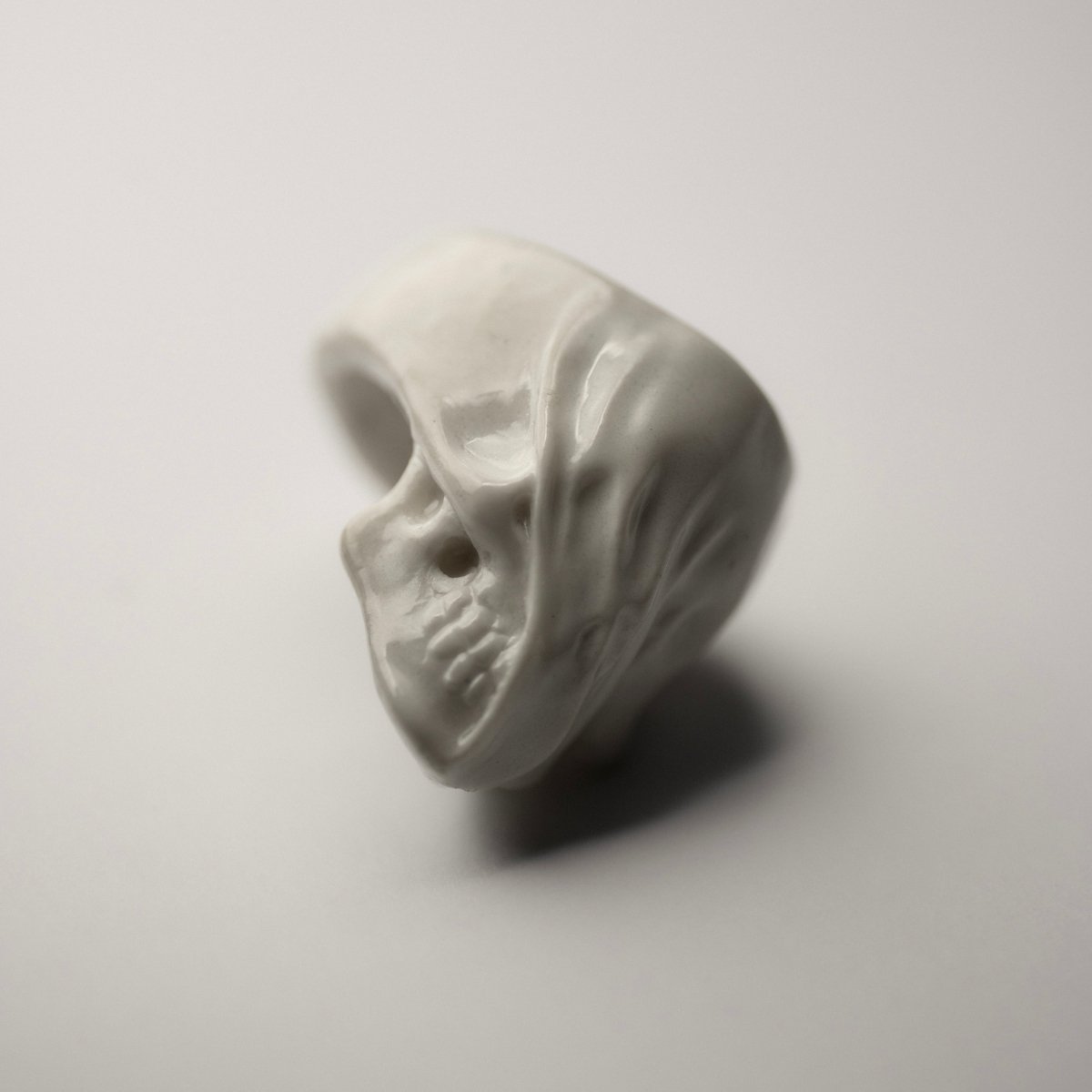 Veiled Skull ring - on a white surface, on its side, focus on glossy finish of the ring