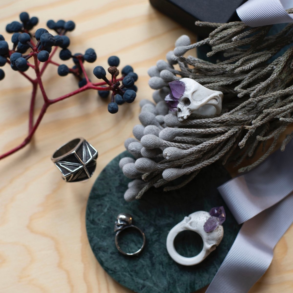 Bifacial Skull Ring along with Amethyst Crystal Skull ring placed on a textured table with flowers, lifestyle