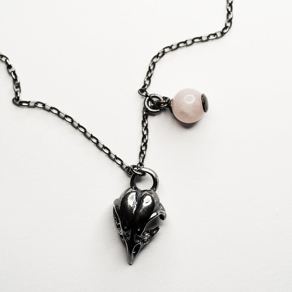 Bird skull charm-pendant placed on a white surface, fixture of a bead and a charm are visible