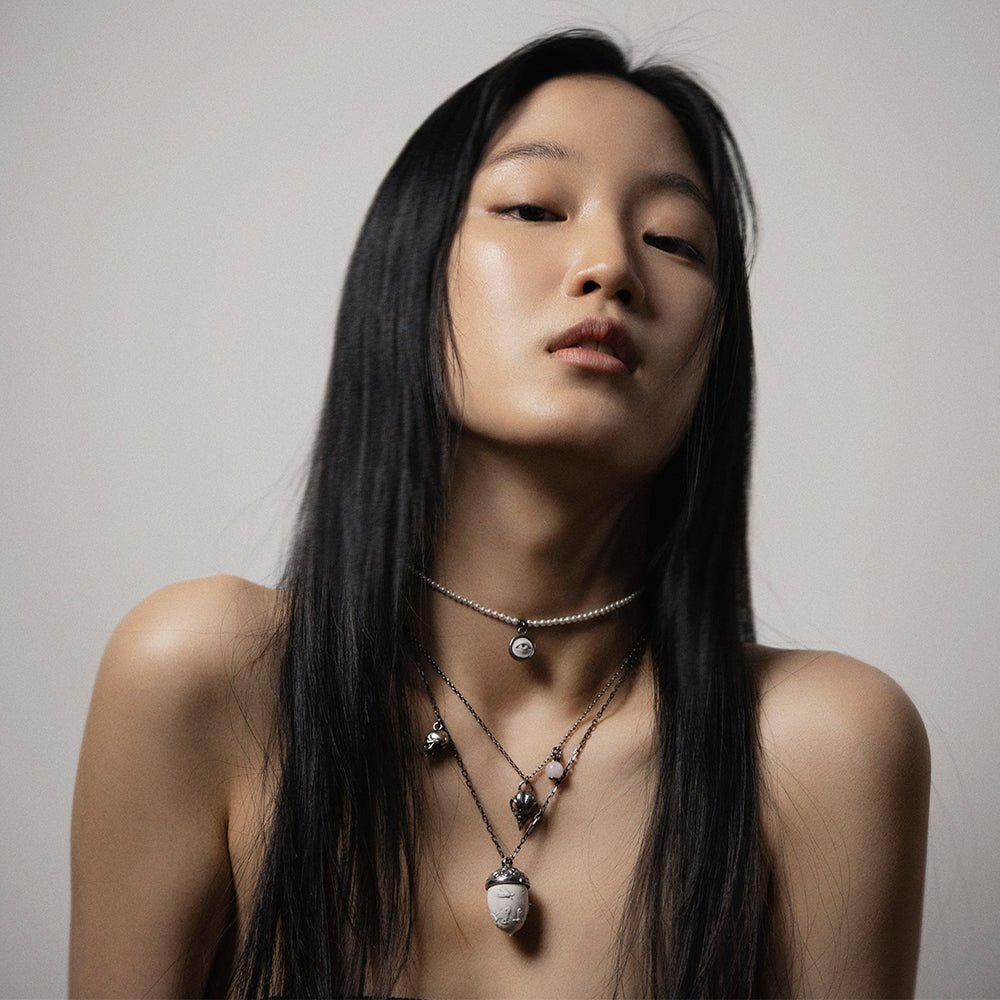Bird skull charm-pendant like one of the strands of multi layered necklace on a female model - semi side view