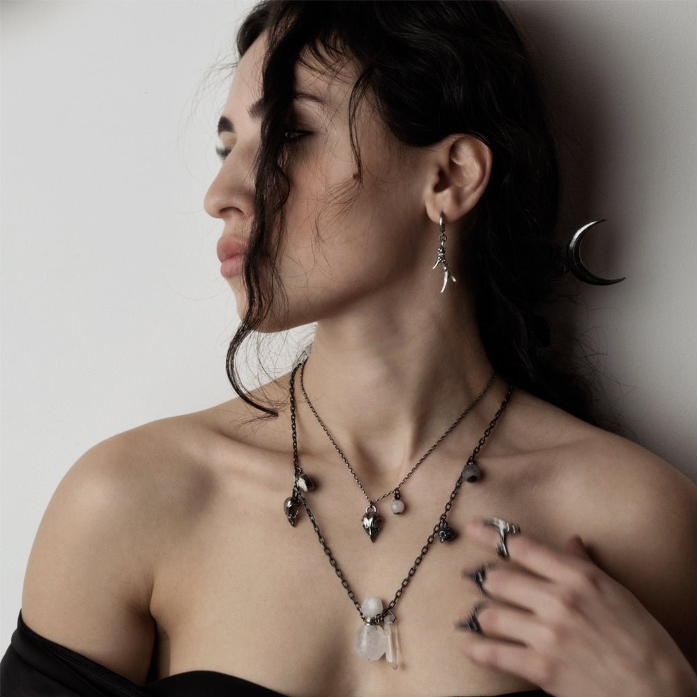 Bird skull charm-pendant on a female model with long dark hair, along with Horn earring by Macabre Gadgets