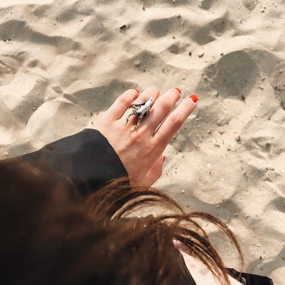 Doe ring on a woman's hand with crimson nails, we can see few locks of brown hair and sand beach, cinematic yet lifestyle image
