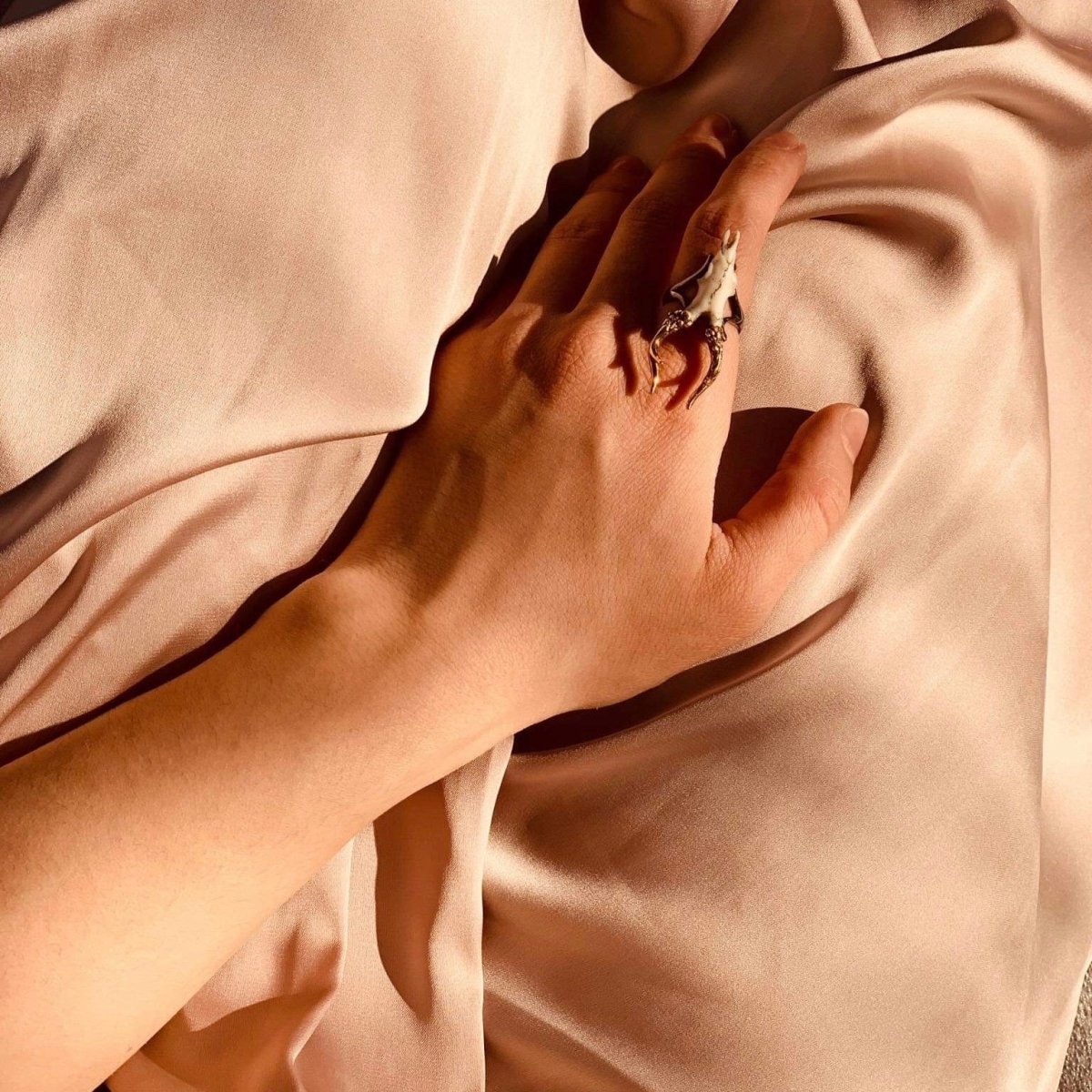 Doe ring on a female model's hand, hand placed on a peachy silk creates elegant folds