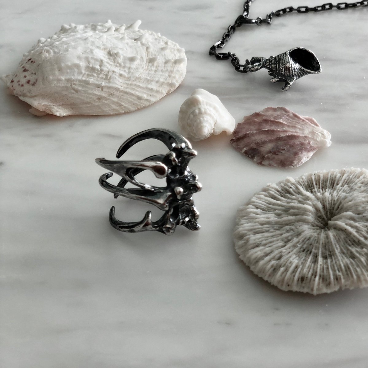 Gills Ribs ring placed on a white marble surface between numerous seashells