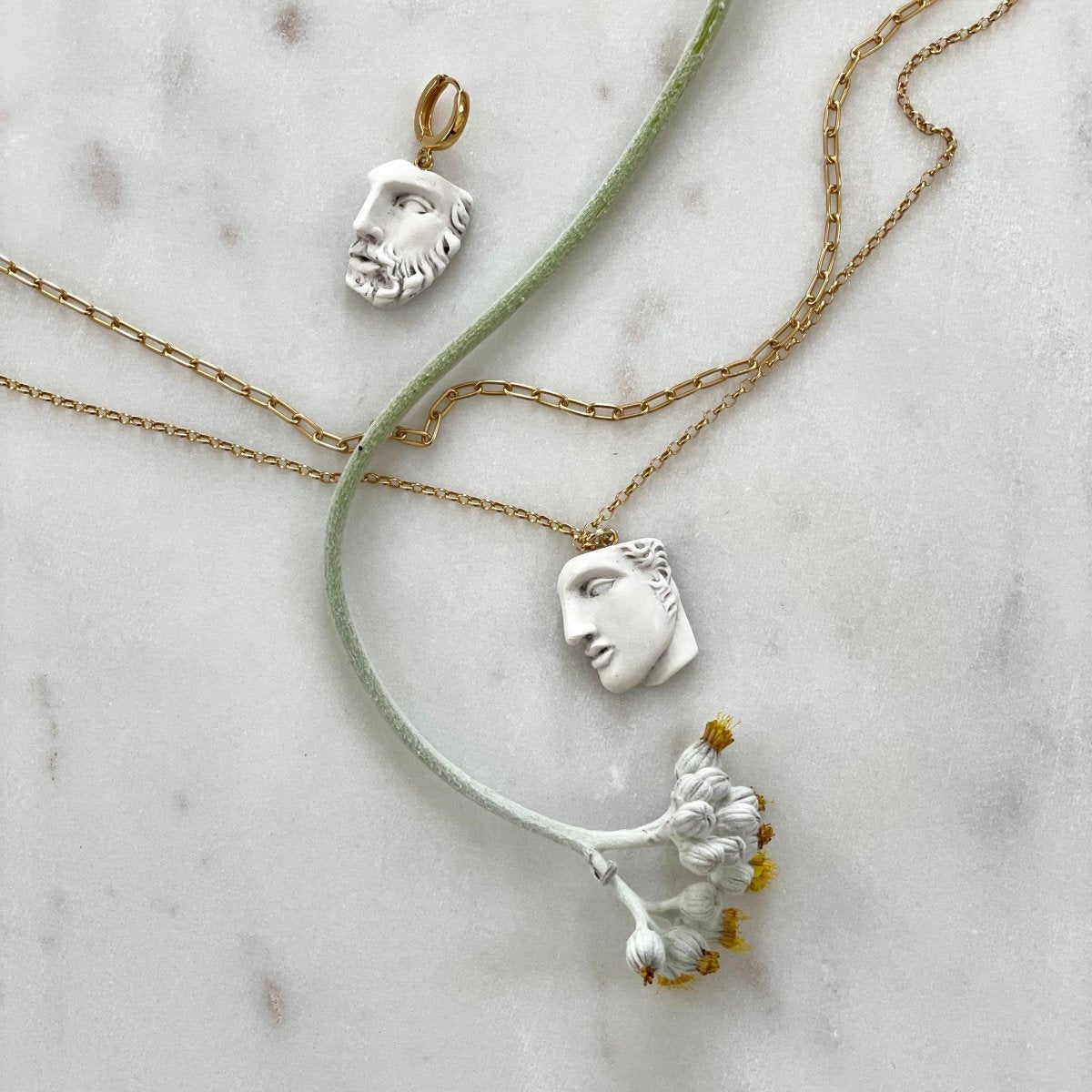 Heracles earring and Achilles pendant on  white marble surface