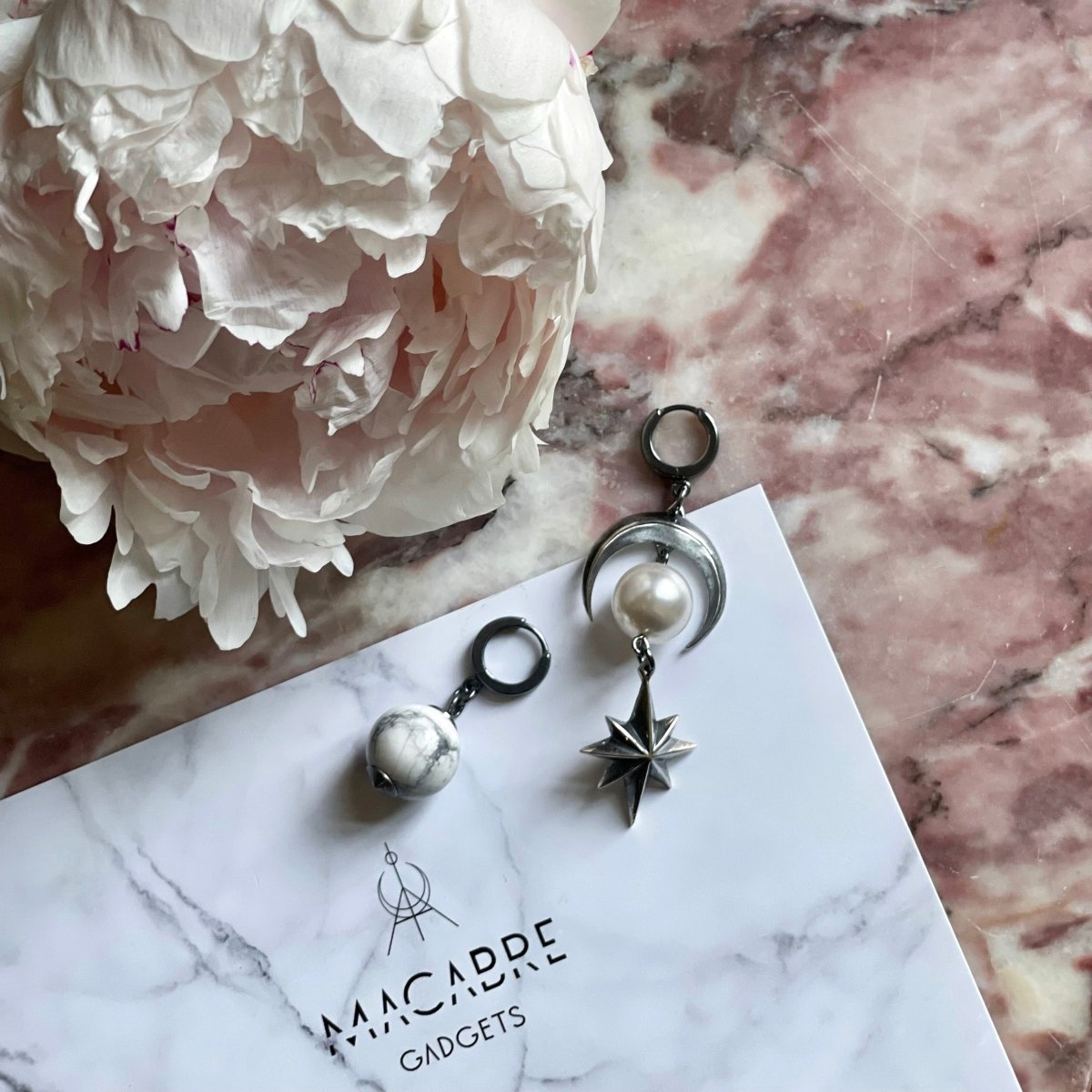Marble Sphere earring and Eclipse earring on rose marble surface aside of large pink peony flower 