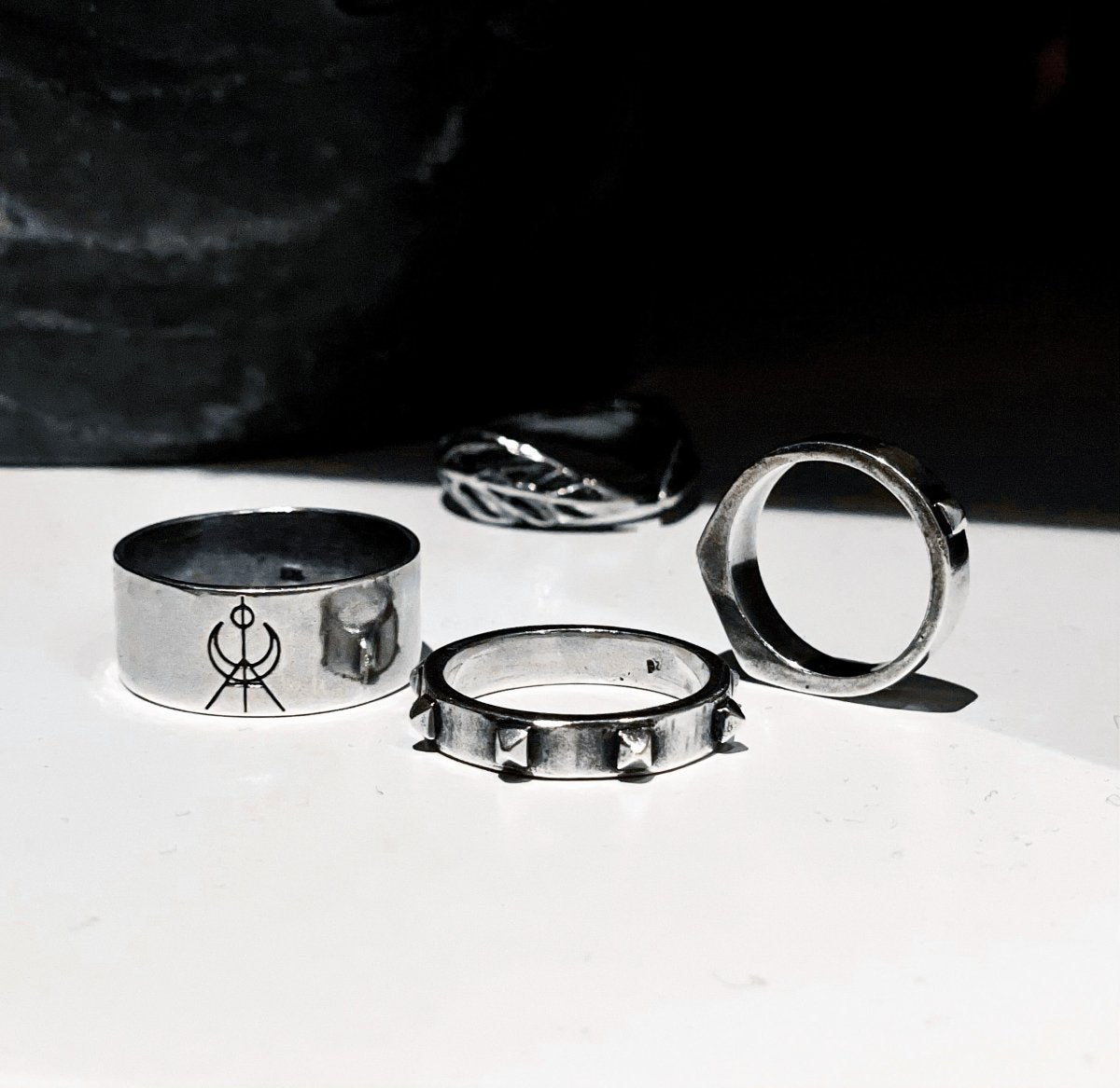 MG Logo ring along with other sterling silver rings by Macabre Gadgets on white surface 
