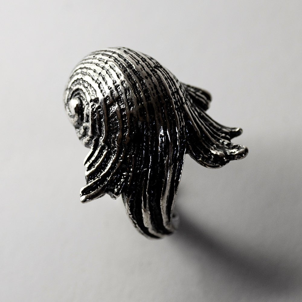 Silver Seashell ring on white surface, focus on shell's texture and its dynamic lines resembling ocean waves