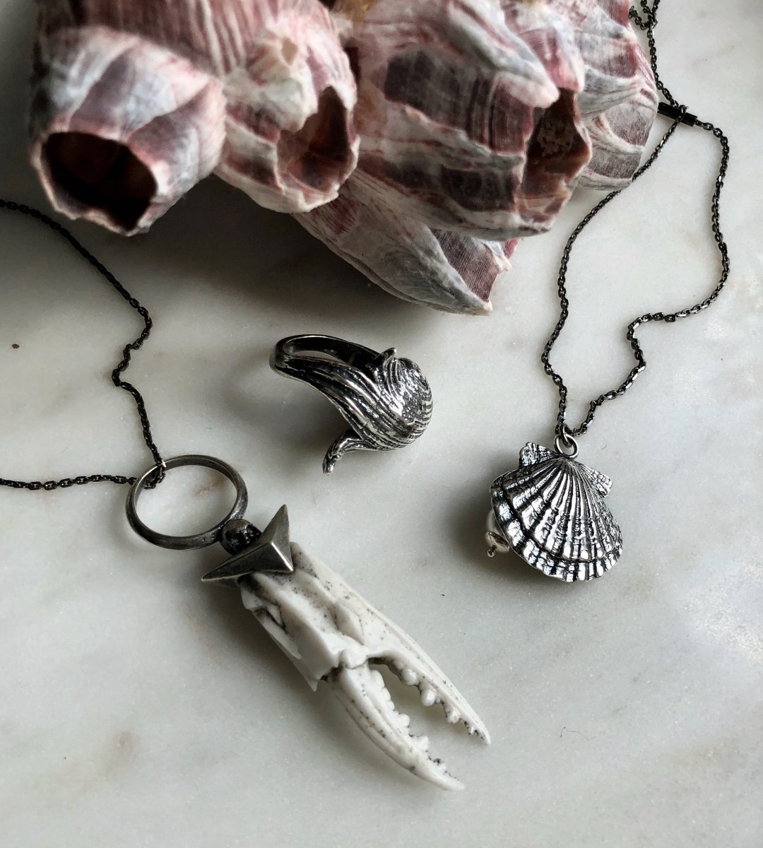 Silver Seashell ring along with other siren core jewelry by Macabre Gadgets on white marble surface