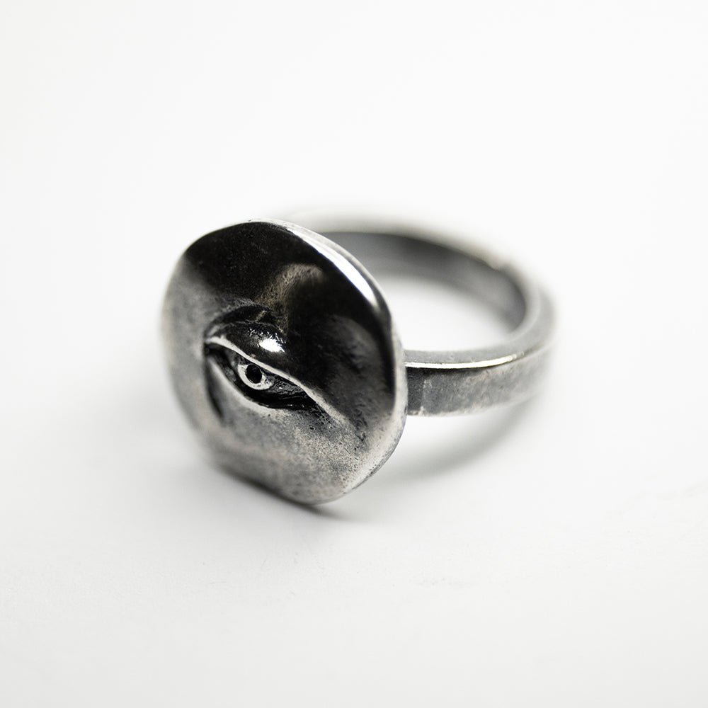 Oculus ring - placed on a white surface, semi side view, focus on eye coin detail