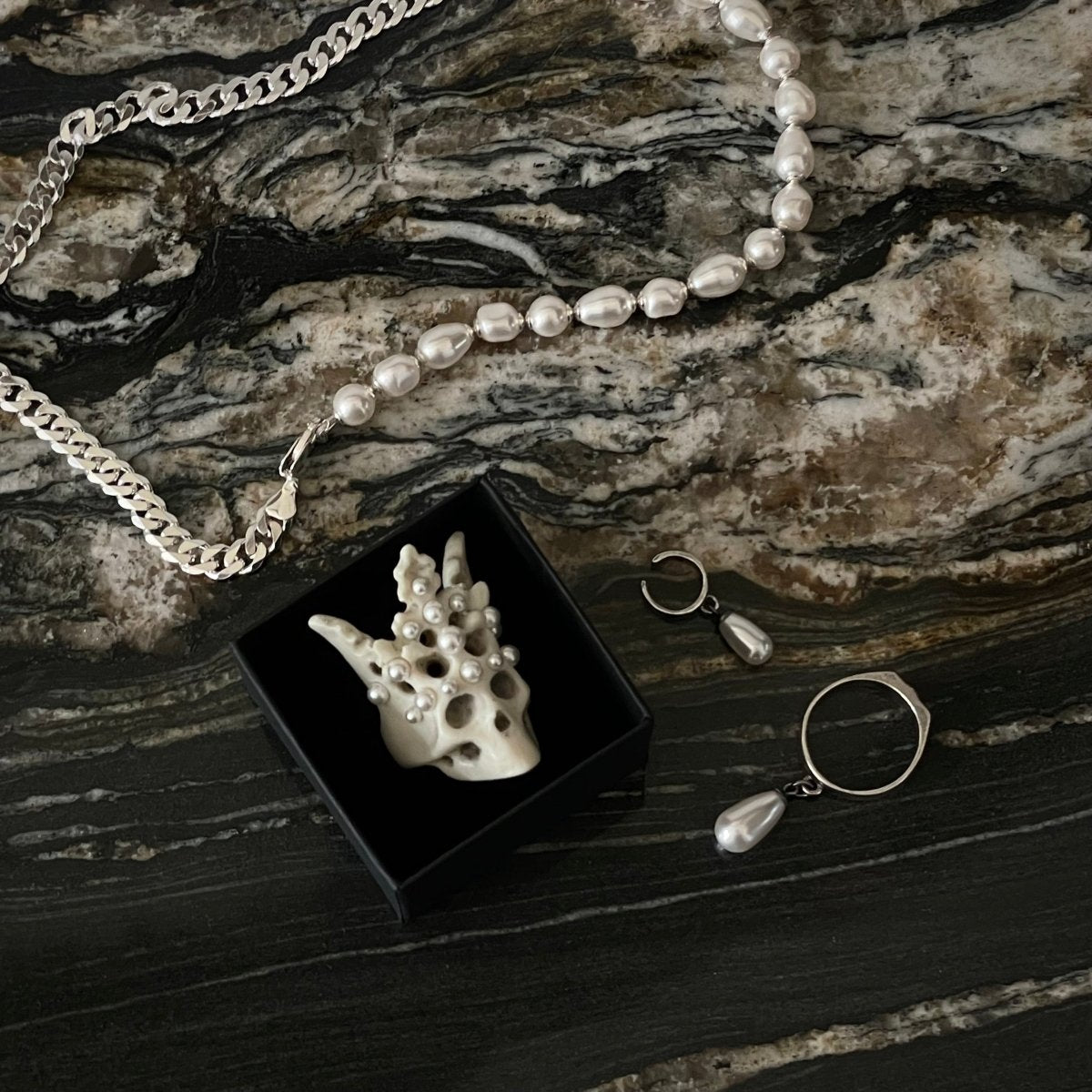 Pearl Crown Skull Ring in a jewelry box along with Double necklace by Macabre Gadgets on marble surface 