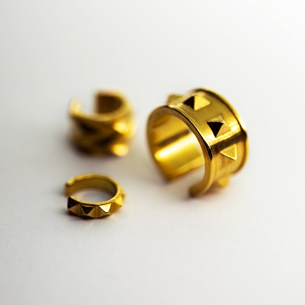 Wide studs ear cuff along with other ear cuffs by Macabre Gadgets in gold-plated finish on neutral surface