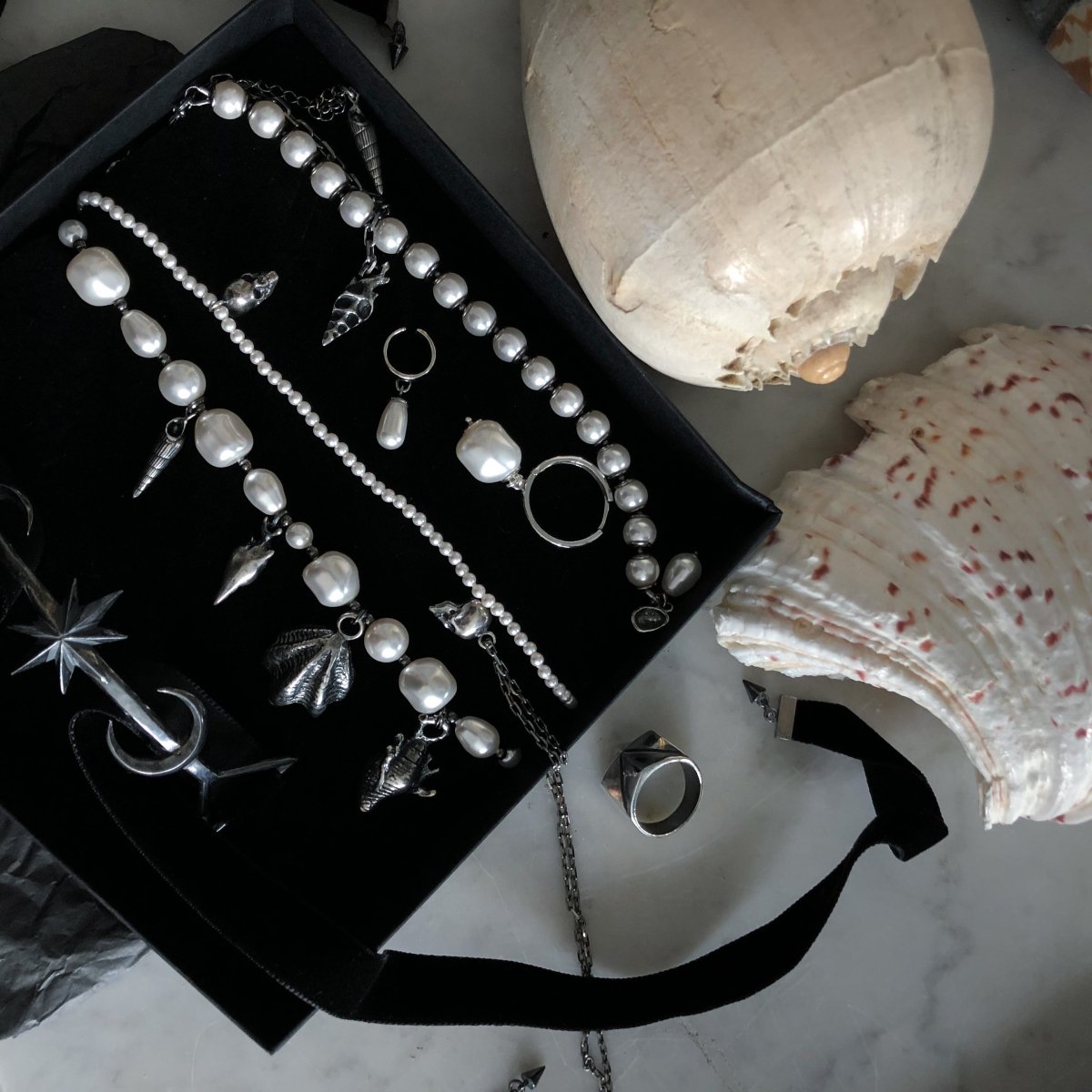Silver Shells and Pearls choker together with other Macabre Gadgets necklaces placed in a large jewelry box on a white marble surface